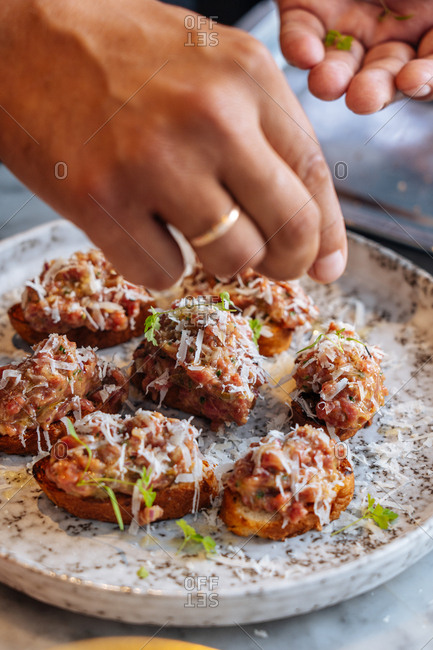 Chef preparing appetizers of small bread slices with meat with cheese