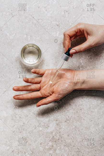 Hands of unrecognisable woman testing cosmetic serum on her skin and holding pipette.