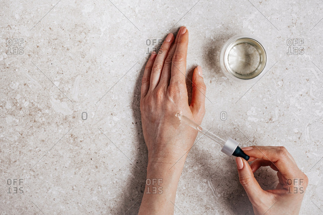 Hands of unrecognisable woman testing cosmetic serum on her skin and holding pipette.