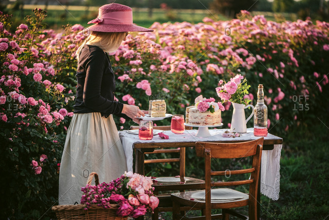 Blonde woman serving cake and wine on an outdoor table in a flower garden