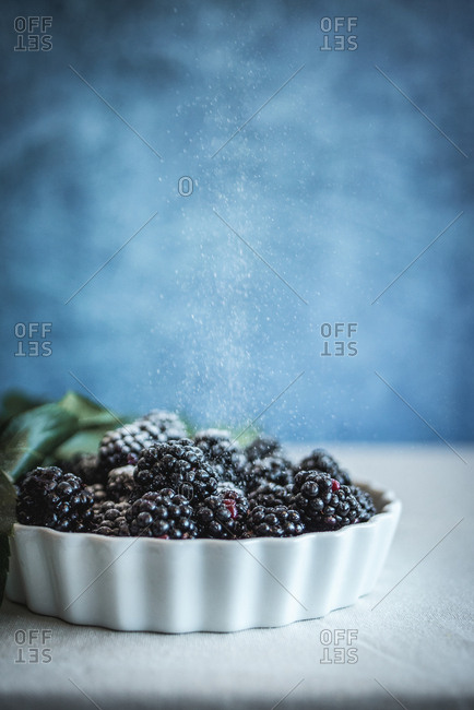 Powdered sugar being sprinkled on dish with blackberries