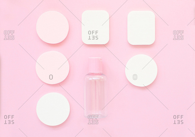 Overhead view of makeup sponges and bottle arranged on a bright pink background