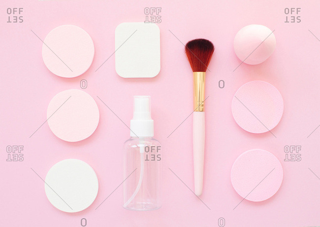 Overhead view of makeup tools and round sponges organized on a bright pink background
