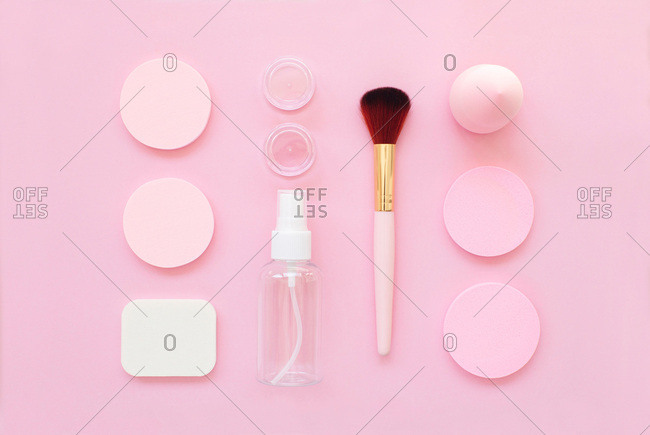 Overhead view of makeup tools organized on a bright pink background
