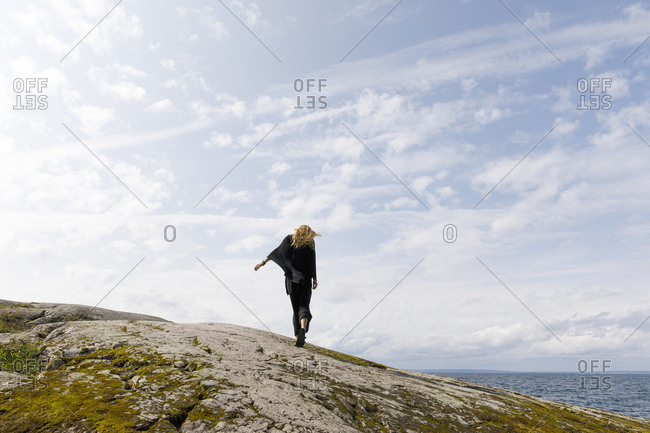 Windswept woman wearing black standing on rock