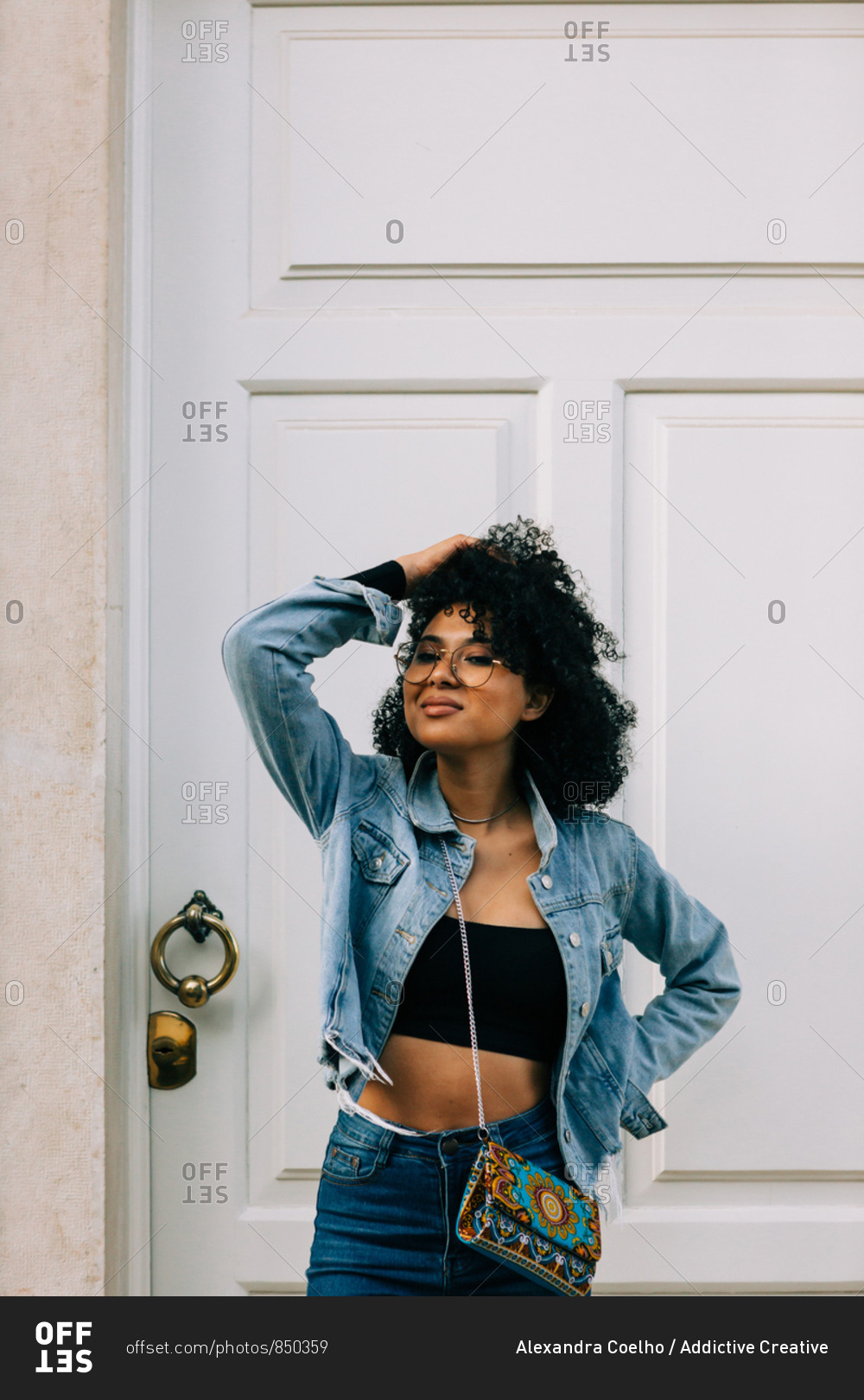 Trendy African American woman in black crop top and jeans standing by door and looking at camera