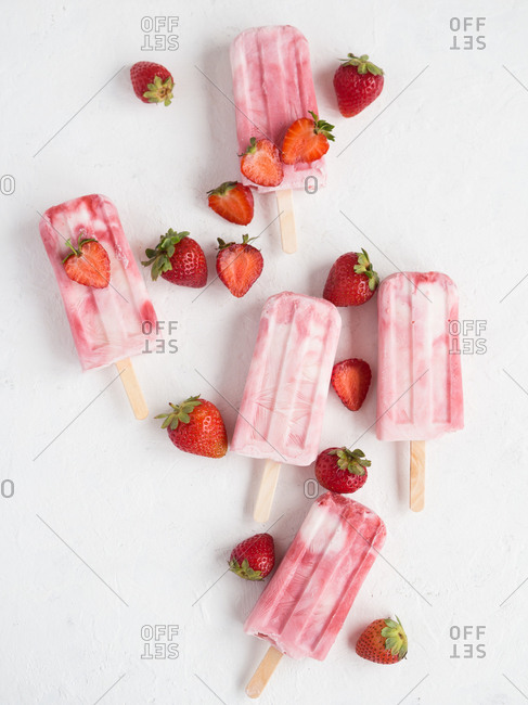 From above delicious refreshing pink freeze pops and bunch of fresh strawberries on white background