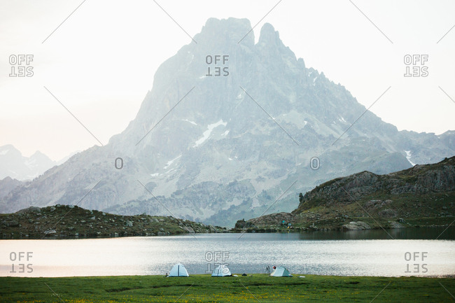 Foggy morning in majestic Pyrenees mountains with travelers tents near clear lake