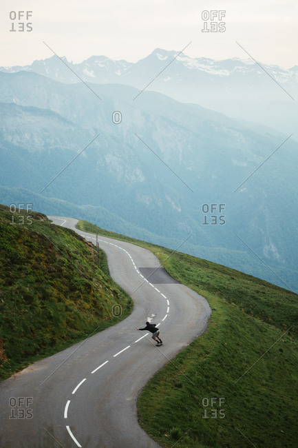 From above morning view of foggy Pyrenees mountains and male traveler skateboarding on serpentine