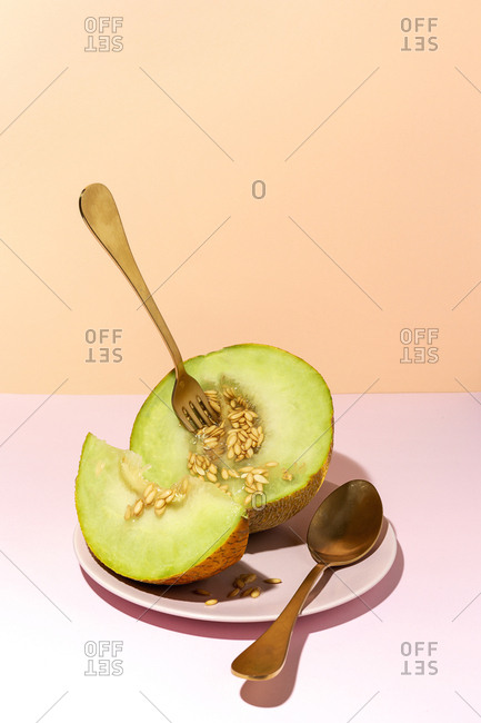 From above cut ripe appetizing sweet pitted melon on plate with spoon and fork in pink table