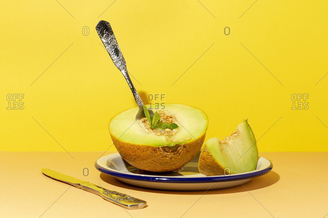 From above cut ripe appetizing sweet pitted melon on plate with spoon and fork in yellow table