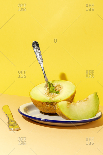 From above cut ripe appetizing sweet pitted melon on plate with spoon and fork in yellow table