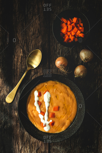 From above tasty fragrant vegetable cream soup with cut ripe carrot and onions on wooden background
