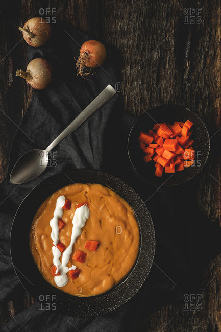 From above tasty fragrant vegetable cream soup with cut ripe carrot and onions on wooden background