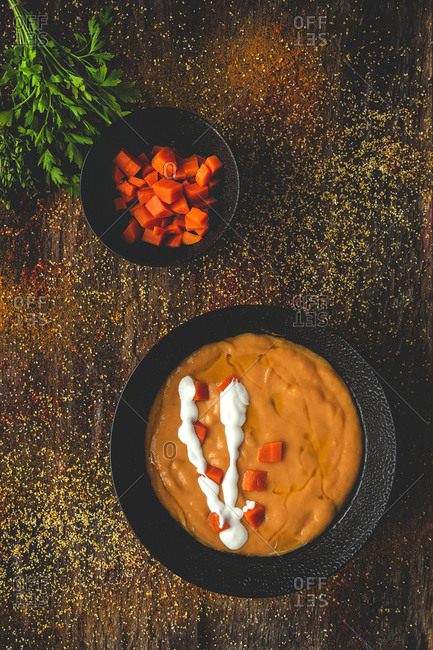 From above tasty fragrant vegetable cream soup with cut ripe carrot and parsley on wooden background