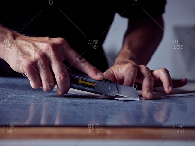 Crop professional man cutting paper sheets with special sharp knife on working table