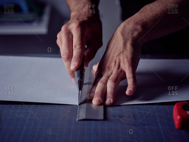 Worker cutting sheet with stationery knife on surface