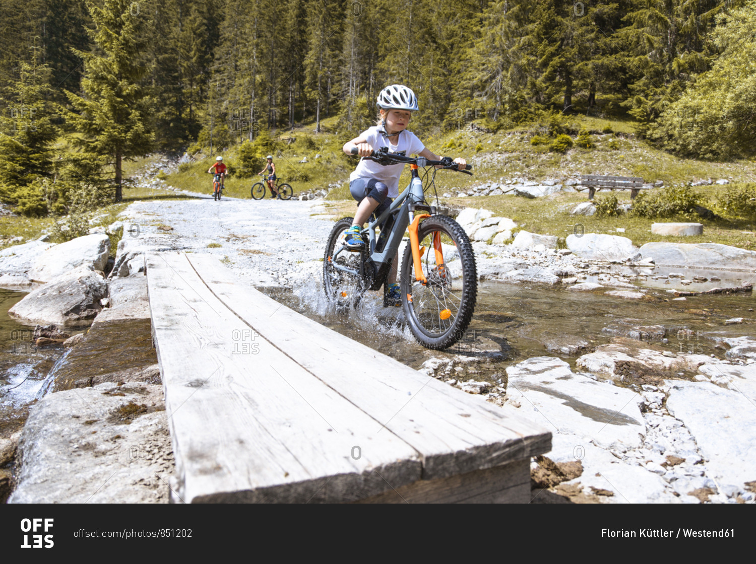 Girl crossing a mountain stream with her e-mountain bike
