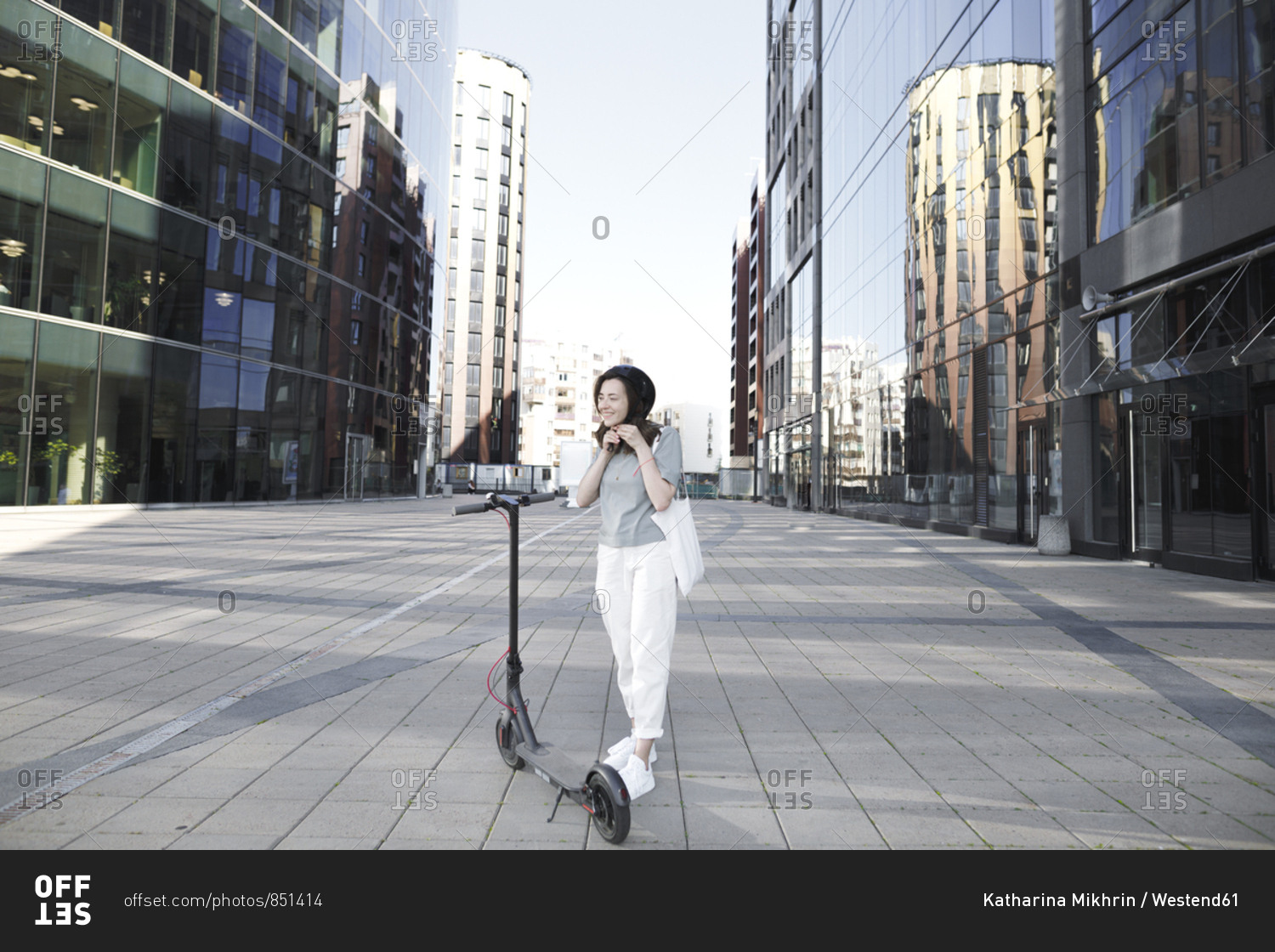 Woman with e-scooter and helmet- modern buildings in the background