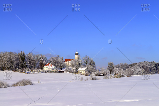 Parish Church of St. Johann Baptist on snow covered landscape against clear blue sky
