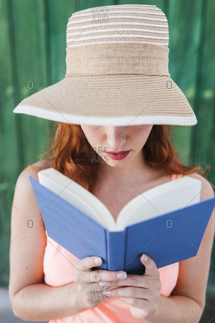 Redheaded Young Woman In Front Of Green Wooden Door Reading