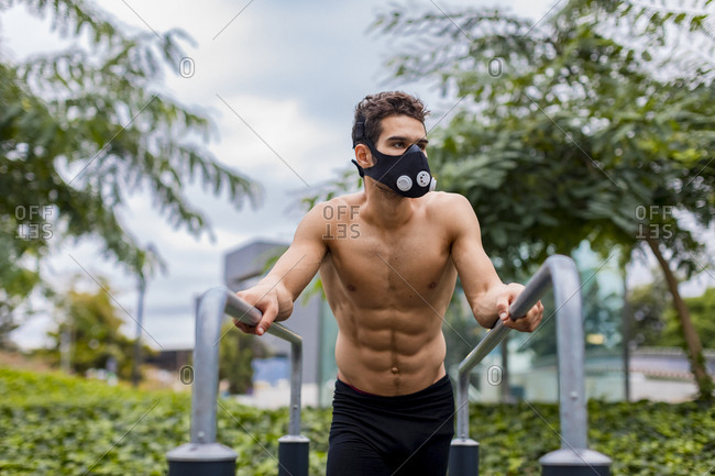 Athlete training on bars in the city- wearing breathing mask