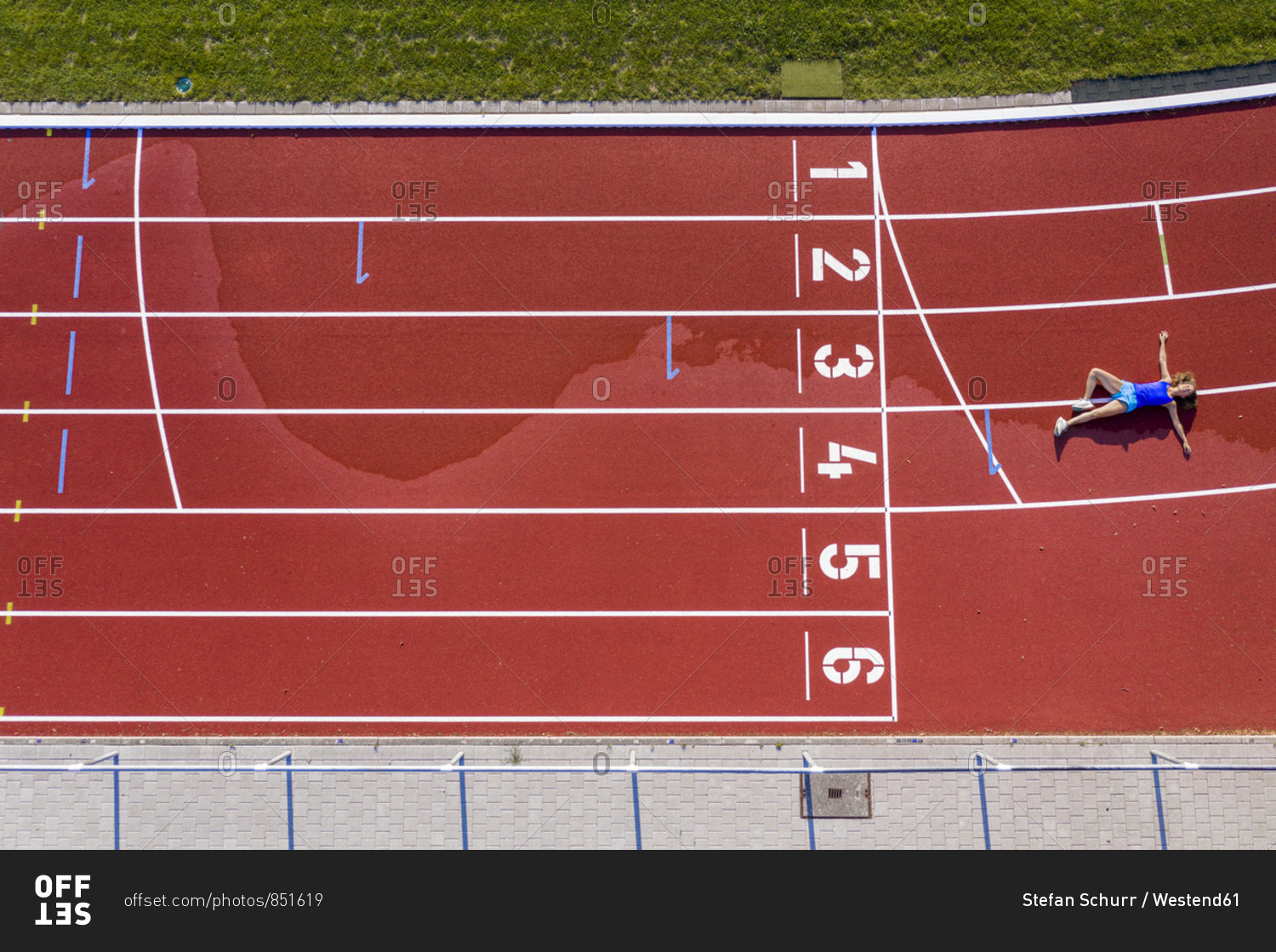 Aerial view of a young female athlete lying on a tartan track after crossing the finishing line