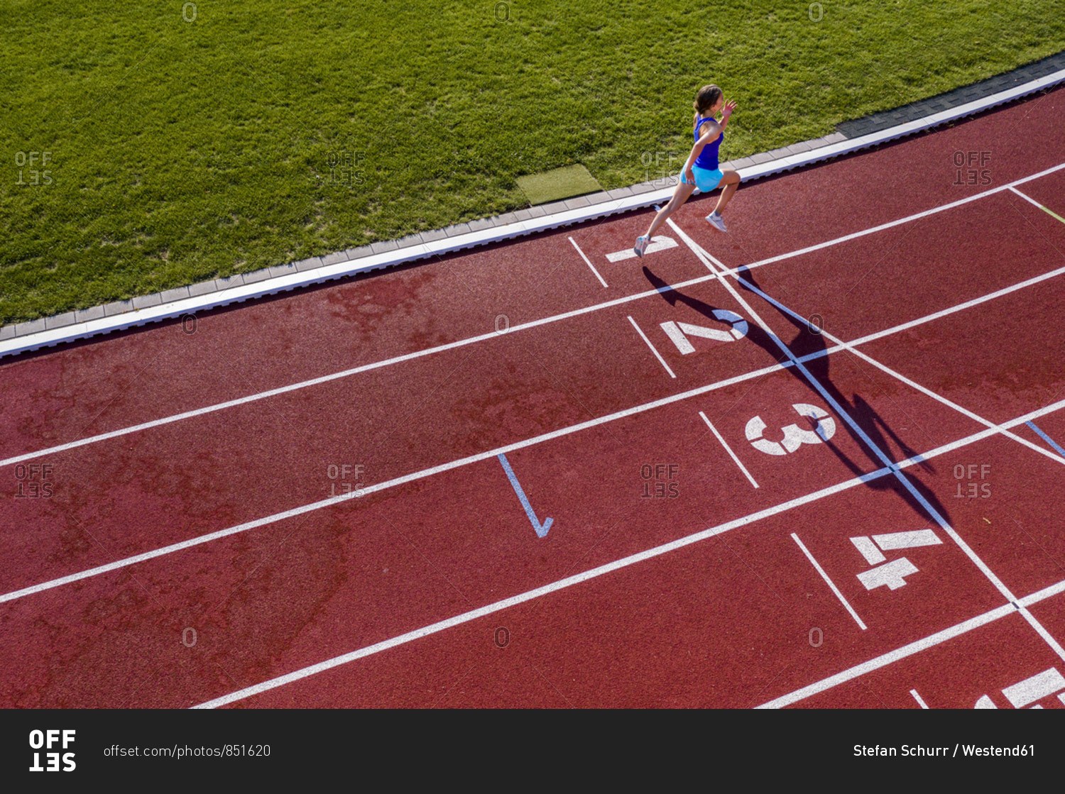 Aerial view of a running young female athlete on a tartan track crossing finishing line