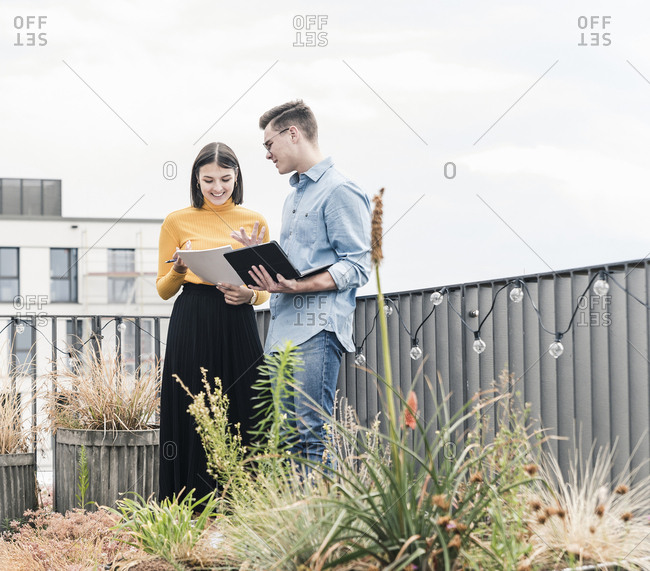 Casual businessman and woman with laptop and documents meeting on roof terrace