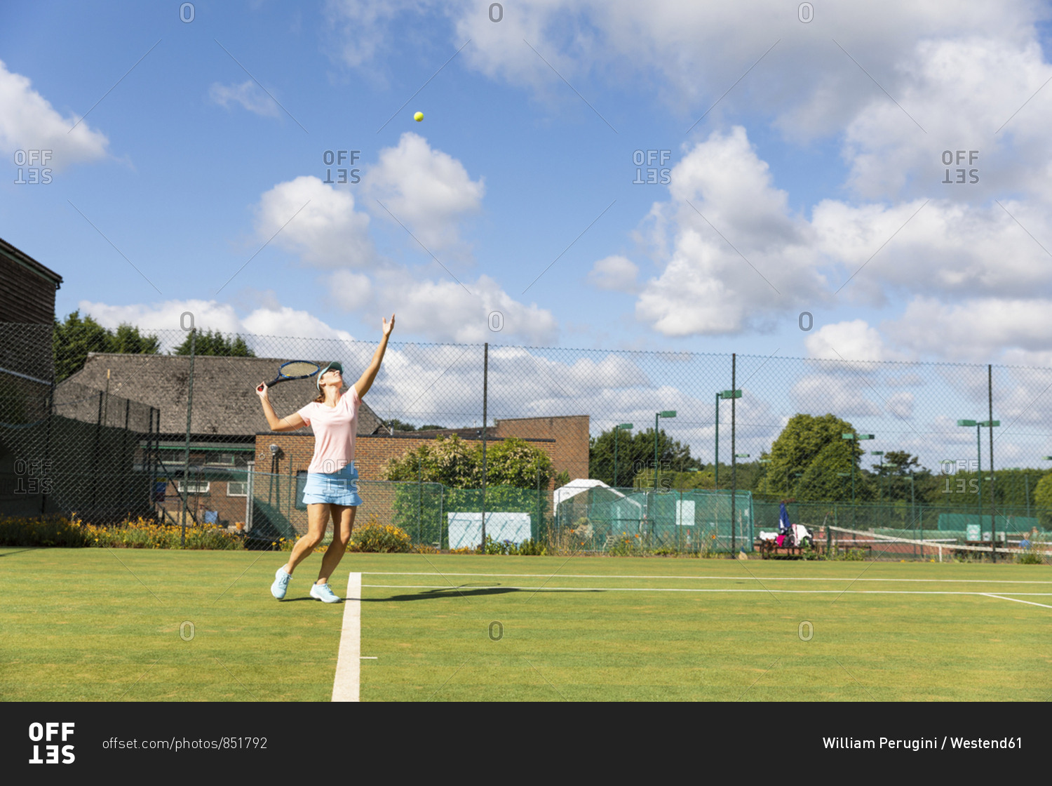 Mature woman serving during a tennis match on grass court