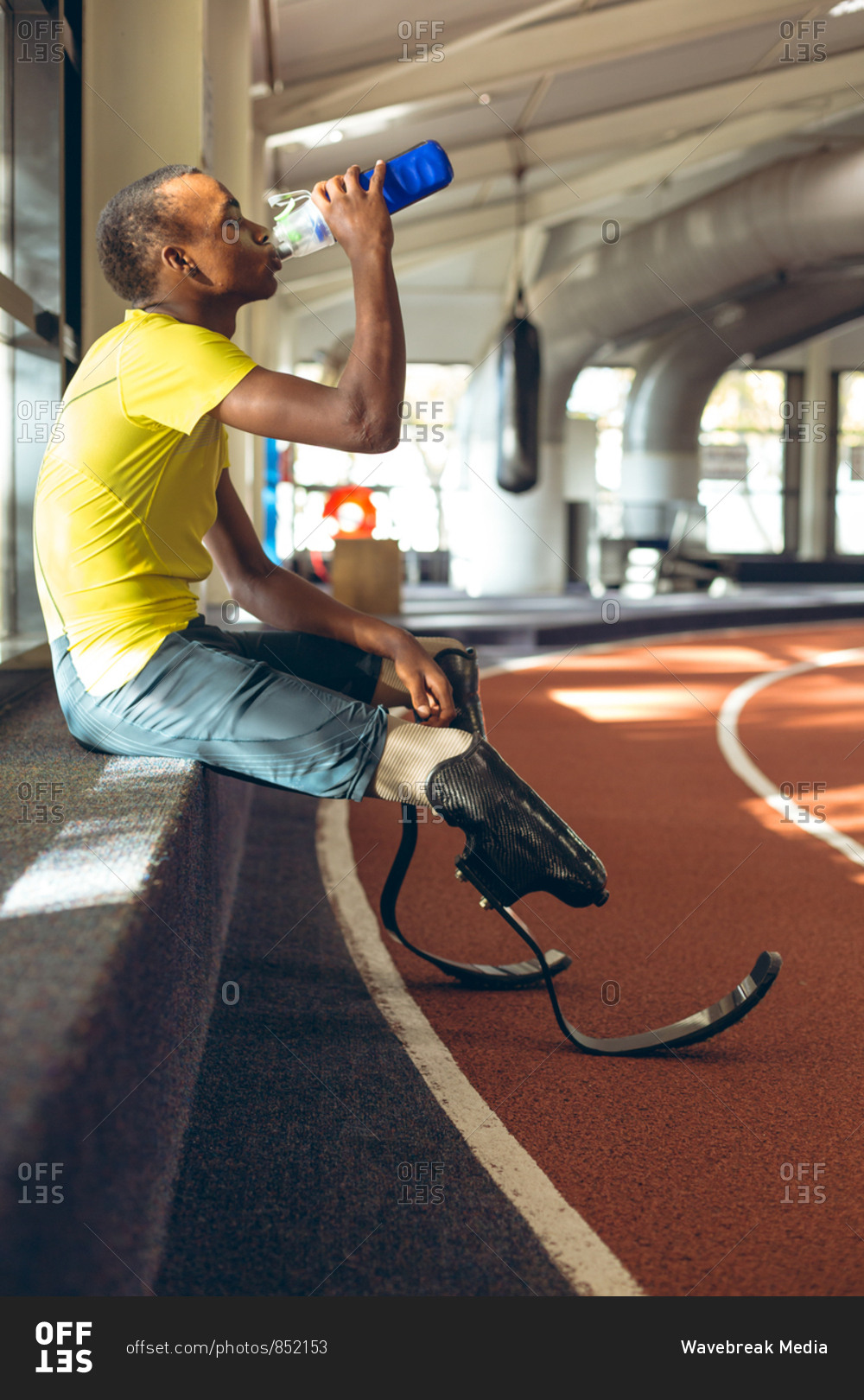 Disabled African American male athletic drinking water on a race track in fitness center
