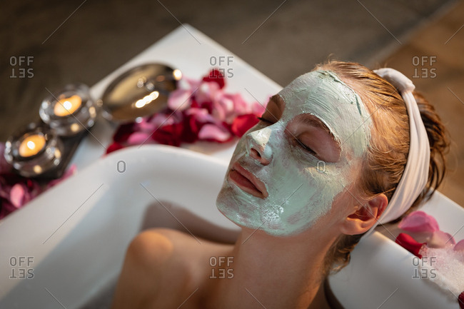 Young blonde woman with face mask relaxing in a bath