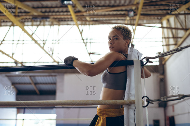 Female boxer leaning on ropes and looking at camera in boxing ring at boxing club