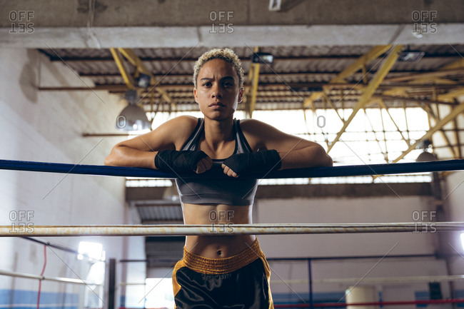 Female boxer leaning on ropes and looking at camera in boxing ring at boxing club