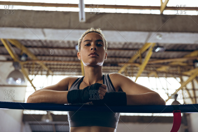 Female boxer leaning on ropes and looking at camera in boxing ring at boxing club