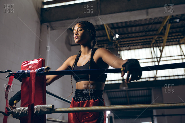 Female boxer with eyes closed leaning on ropes in boxing ring at boxing club