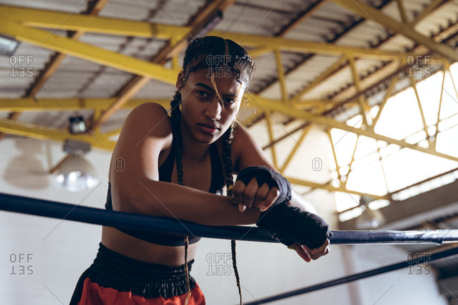Female boxer leaning on ropes and looking at camera in boxing ring at boxing club