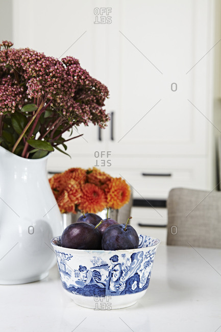 Plums in bowl on counter by flowers