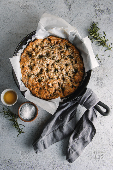 baked rosemary focaccia served in a cast iron skillet with handle wrapped in linen cloth, served alonside sea salt and olive oil