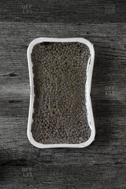 Hiigh angle view of a vacuum packed plastic container with some cooked lentils, on a wooden surface