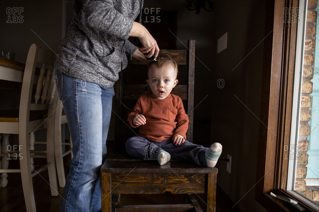 Mom cutting young boys hair sitting on a chair by the window