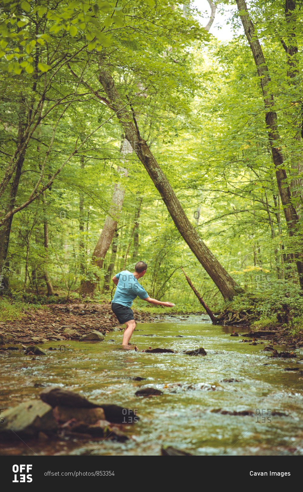 A young male throws a rock down stream while standing in a river.