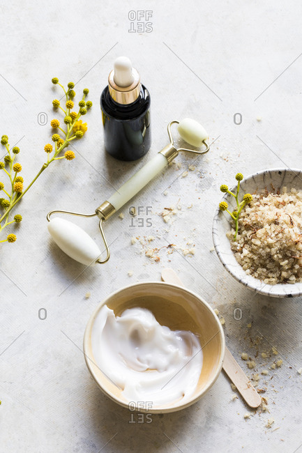 Two bowls of natural skin care products with yellow flowers and facial roller