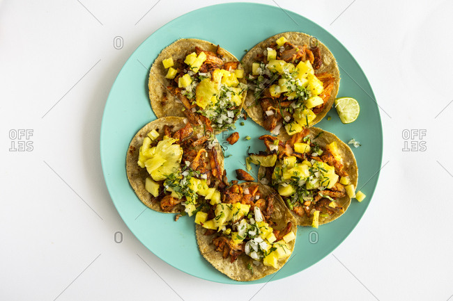 Overhead view of al pastor tacos with pineapple, coriander, onion and lemon