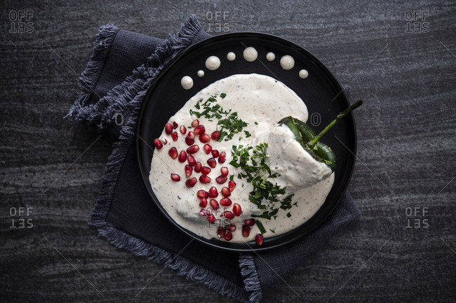 Overview of chile in nogada with cream and pomegranate over a black wooden background