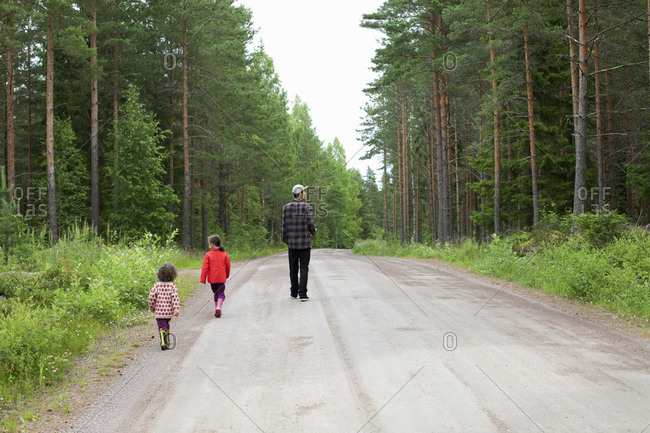 Man and children walking on rural road through forest