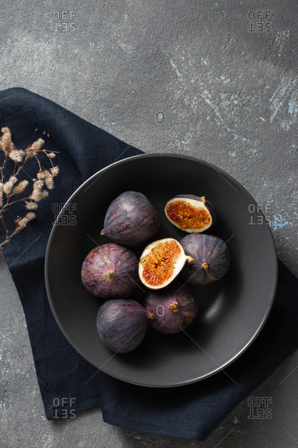 Overhead view organic sliced and whole fresh figs in bowl on dark background