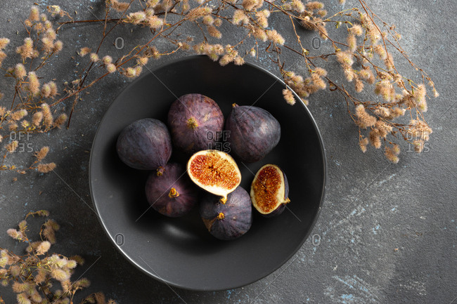 Organic sliced and whole fresh figs in bowl on dark background