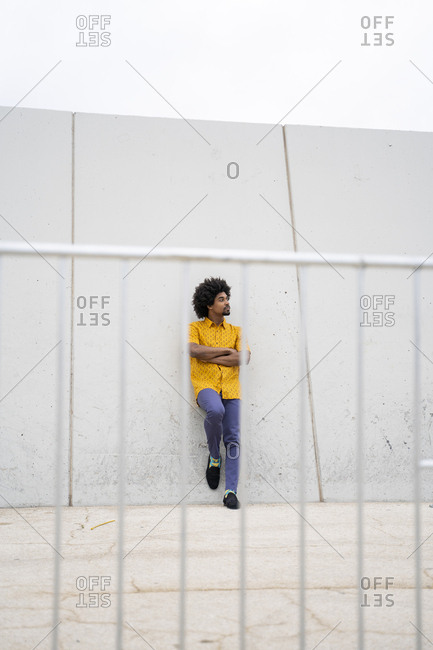 Young hipster wearing yellow shirt- looking sideways- leaning on a white wall