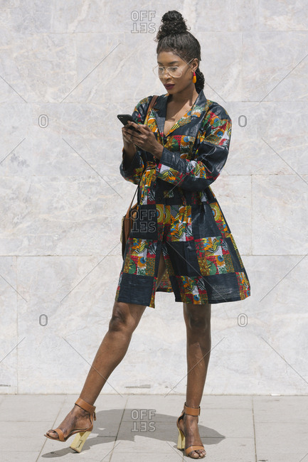 Portrait of chic woman wearing patterned dress using cell phone